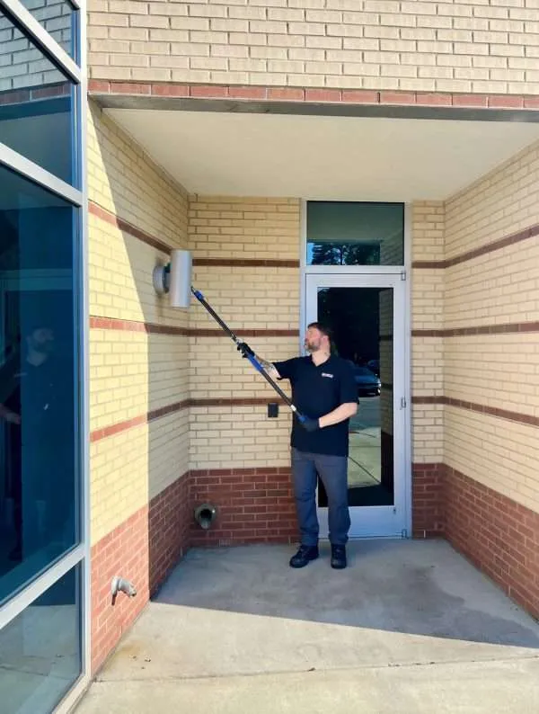 Complete Pest Management technician removing spider webs from building eaves in Hampton Roads